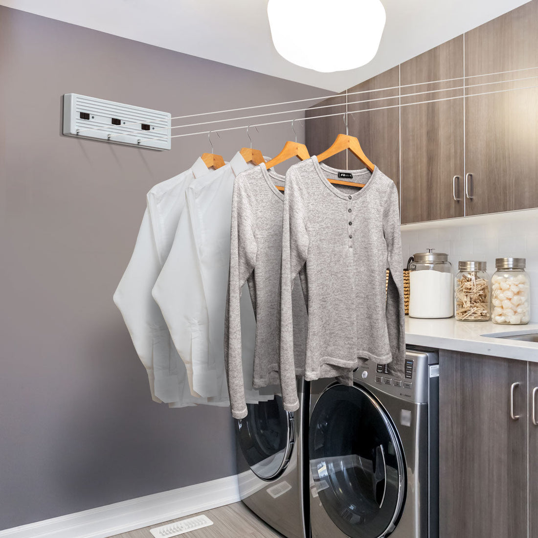 Cuarto de lavado moderno con tendedero retráctil Tensoline extendido y camisas secándose en ganchos